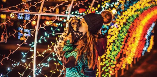 A visitor kissing a small dog inside the tunnel of lights.